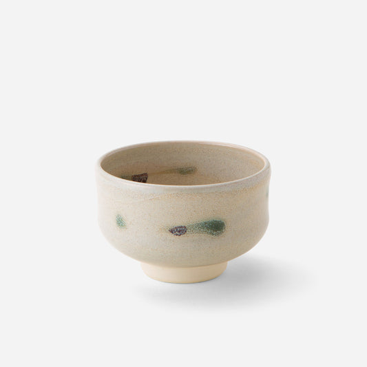 Handcrafted Japanese tea bowl with rustic tricolor glaze, featuring subtle green and brown brushstrokes on a creamy base, embodying wabi-sabi aesthetics