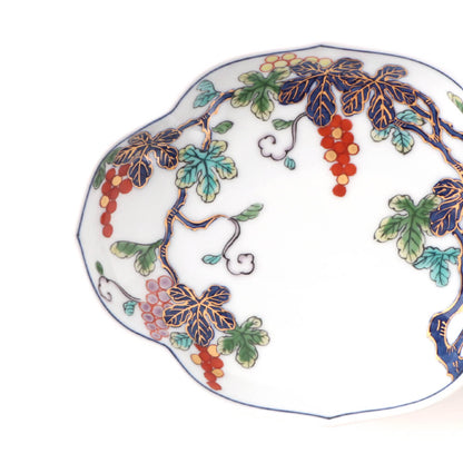 Handcrafted Japanese oval plate featuring intricate grapevine design with purple leaves, red grapes, and green accents on a white background with scalloped edges