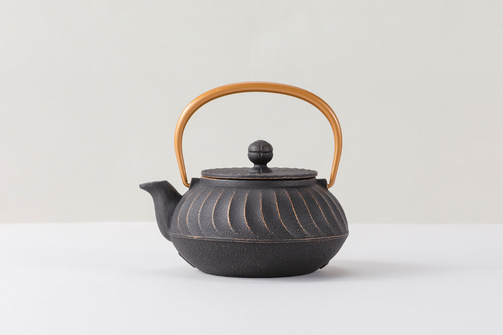 Japanese Kyusu Gata Nami cast iron teapot featuring a black body with intricate gold wave patterns and a curved golden handle, embodying traditional craftsmanship