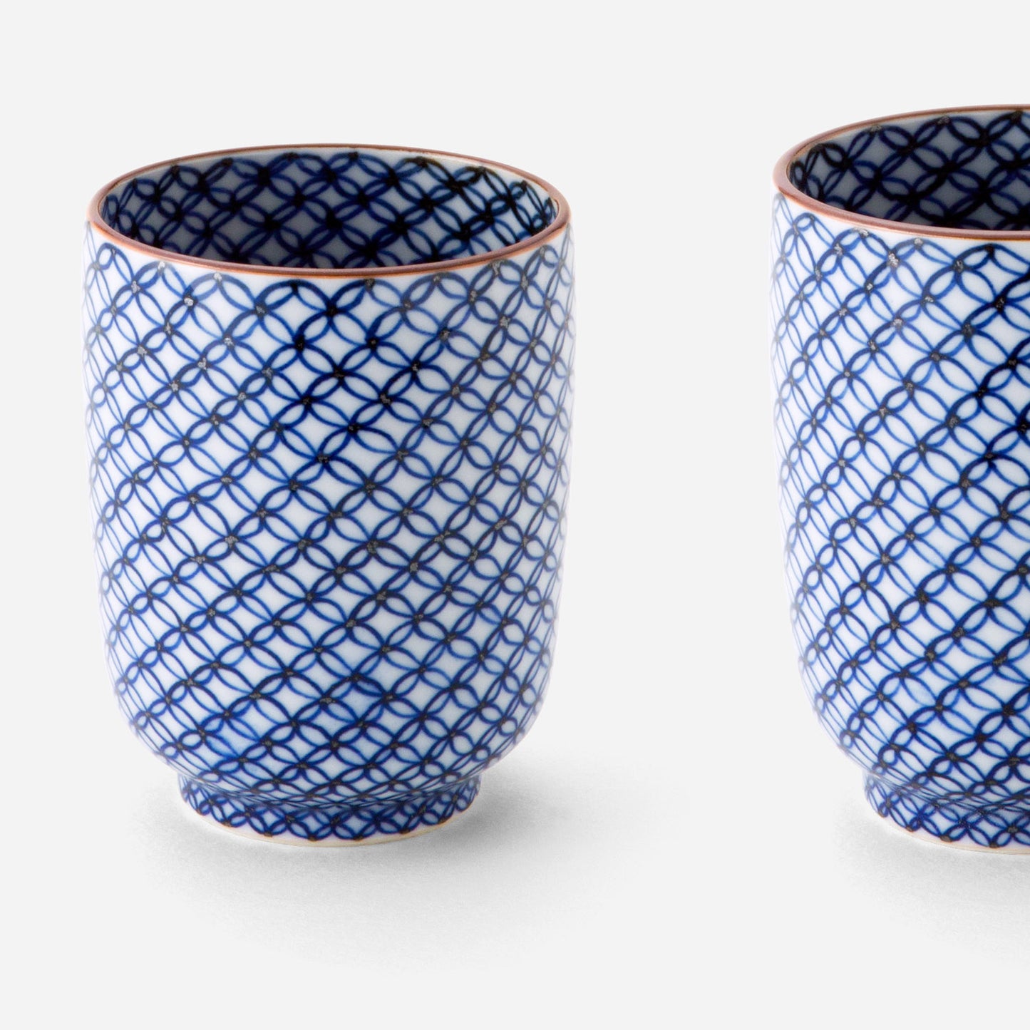 Handcrafted Japanese teacup set with blue sometsuke shippo pattern, featuring two cups with intricate designs of overlapping circles in cobalt blue on a white background with copper-colored rims