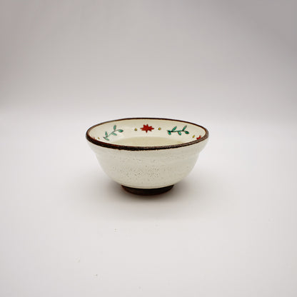 Small ceramic bowl with hand-painted red flowers and green leaves around the rim, featuring a creamy interior and rustic brown edge