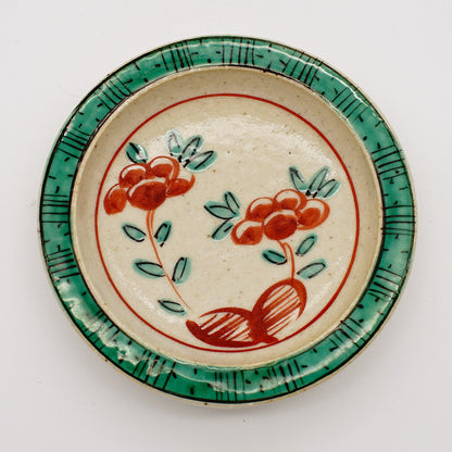 Small ceramic dish with hand-painted red flowers and green border, showcasing traditional Japanese akae style artwork