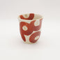 Creamy white Shino tea cup with bold crimson camellia-inspired brushstrokes and gold accents, showcasing modern Japanese ceramic artistry