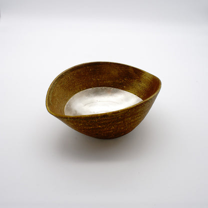 Asymmetrical ceramic bowl with golden-brown exterior and silver interior, showcasing a unique sunset-inspired shape and metallic finishes